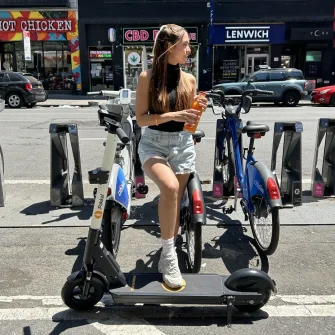 Rider on a Ride by iPakket e-scooter next to a bike dock on a city street