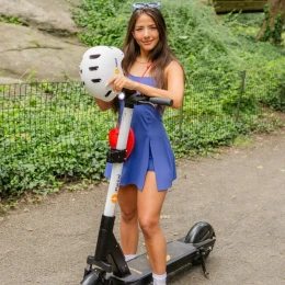 Rider holding a safety helmet beside an iPakket e-scooter in the park