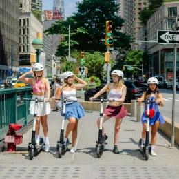 Four riders lined up with helmets along an urban sidewalk