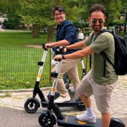 Two riders on iPakket e-scooters smiling on a park path